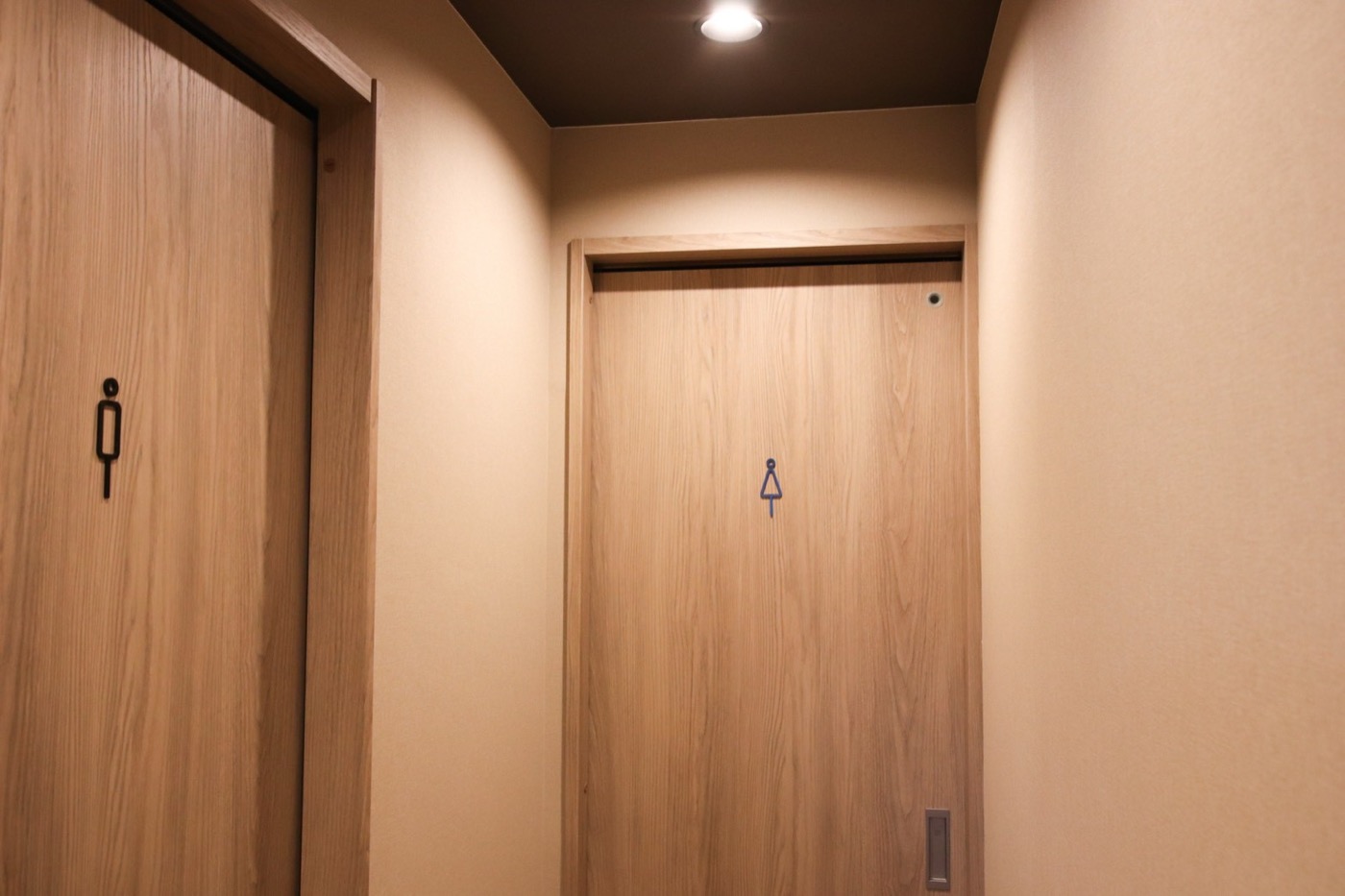 ライトウッドドアにアイアン製ピクトグラム取手を添えた、清潔感あるトイレ廊下